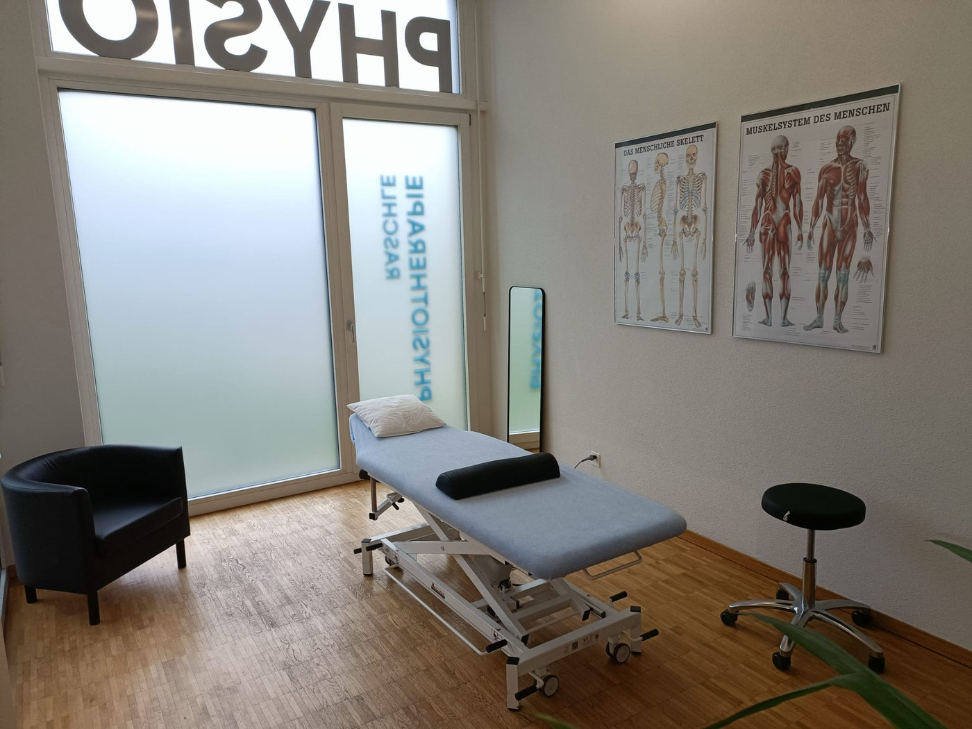 Heller Behandlungsraum mit Therapieliege und Anatomie-Postern