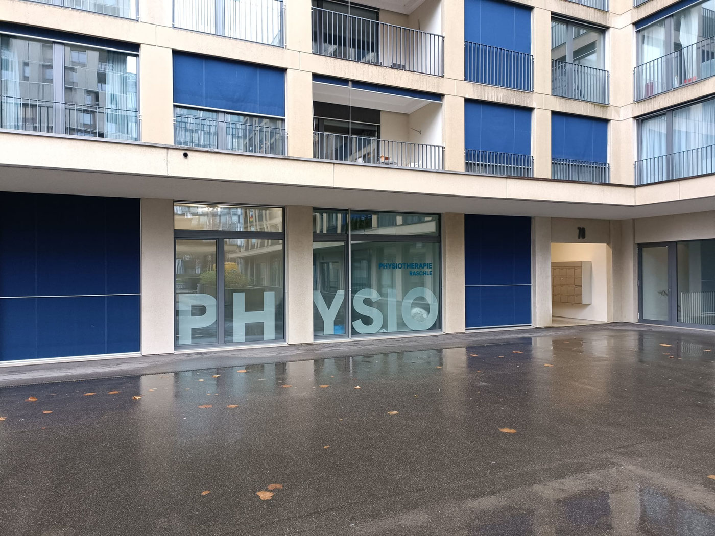 Eingang der Physiotherapie Raschle an der Hagenholzstrasse 70 mit grosser PHYSIO-Fensterbeschriftung